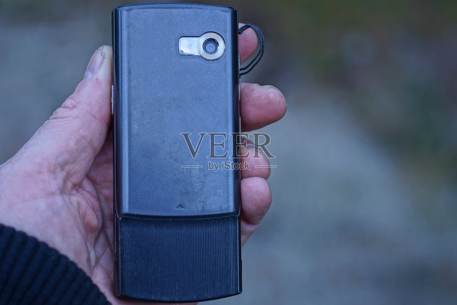 手里拿着一部带摄像头的黑色旧手机照片摄影图片