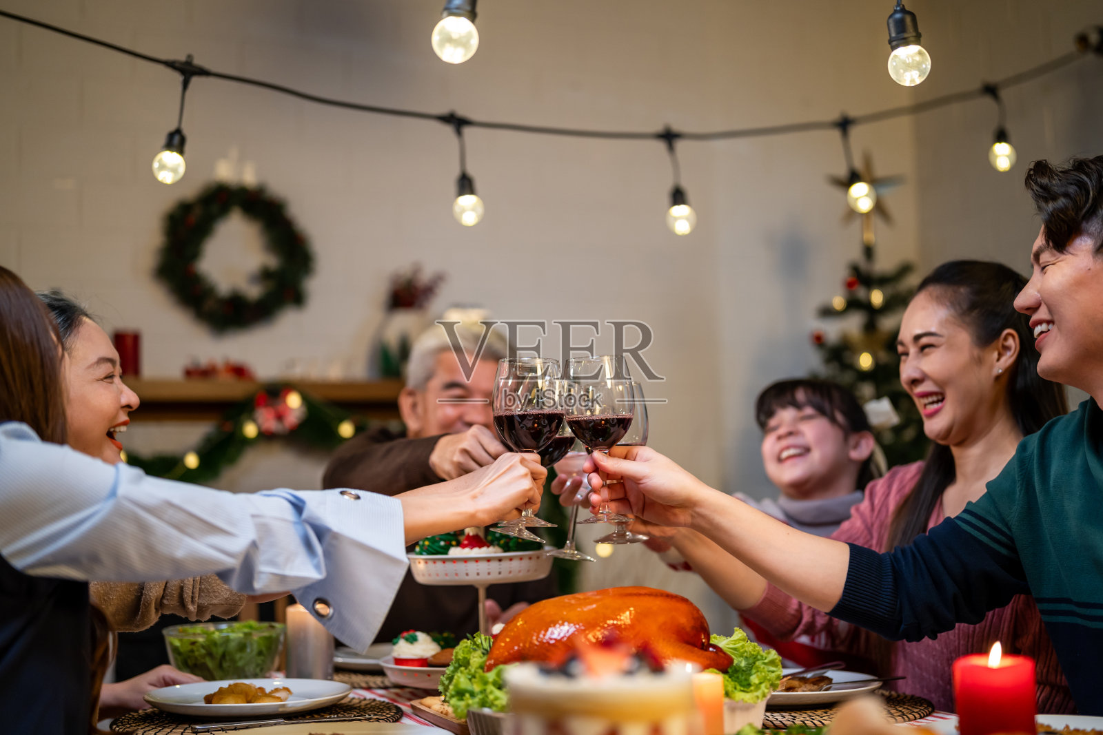 亚洲可爱的家庭在家里一起庆祝圣诞派对。迷人的父母和亲戚们共进晚餐,举杯共庆感恩节,平安夜的餐桌上照片摄影图片