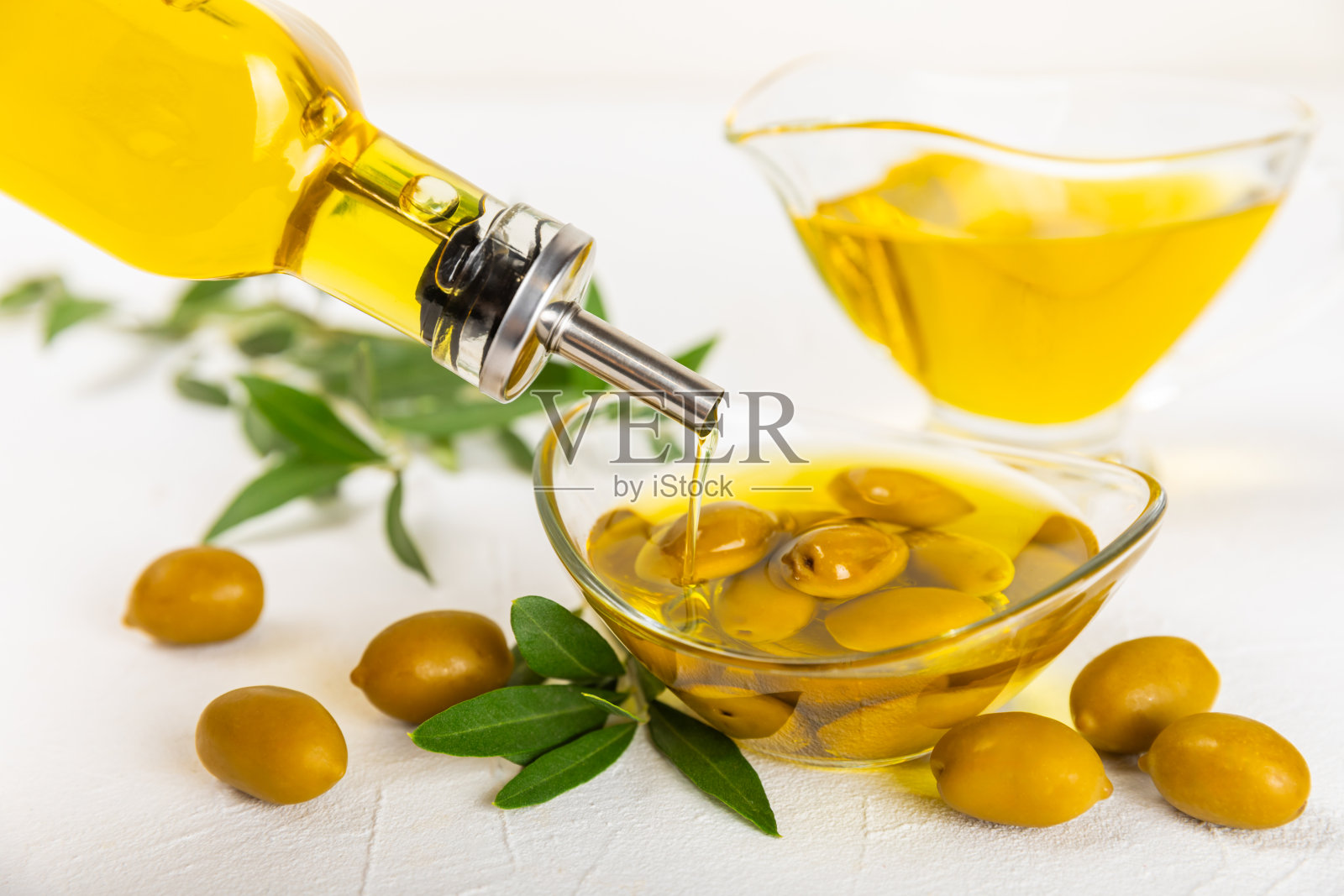 白色纹理背景上的一瓶橄榄油。油瓶上有树枝和橄榄果实。放文字的地方。副本的空间。食用油和沙拉酱。照片摄影图片