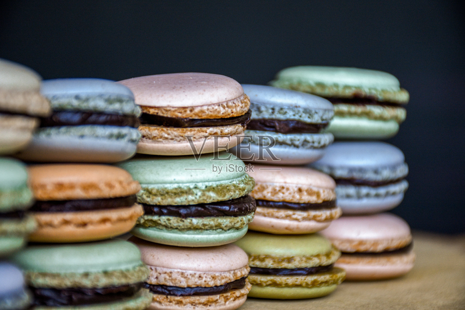 在黑暗的背景上堆叠着甜美多彩的马卡龙饼干。照片摄影图片