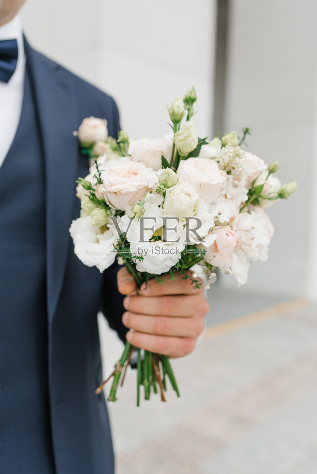 身穿蓝色西装的新郎手里拿着一束精致的婚礼花束,送给他心爱的新娘照片摄影图片
