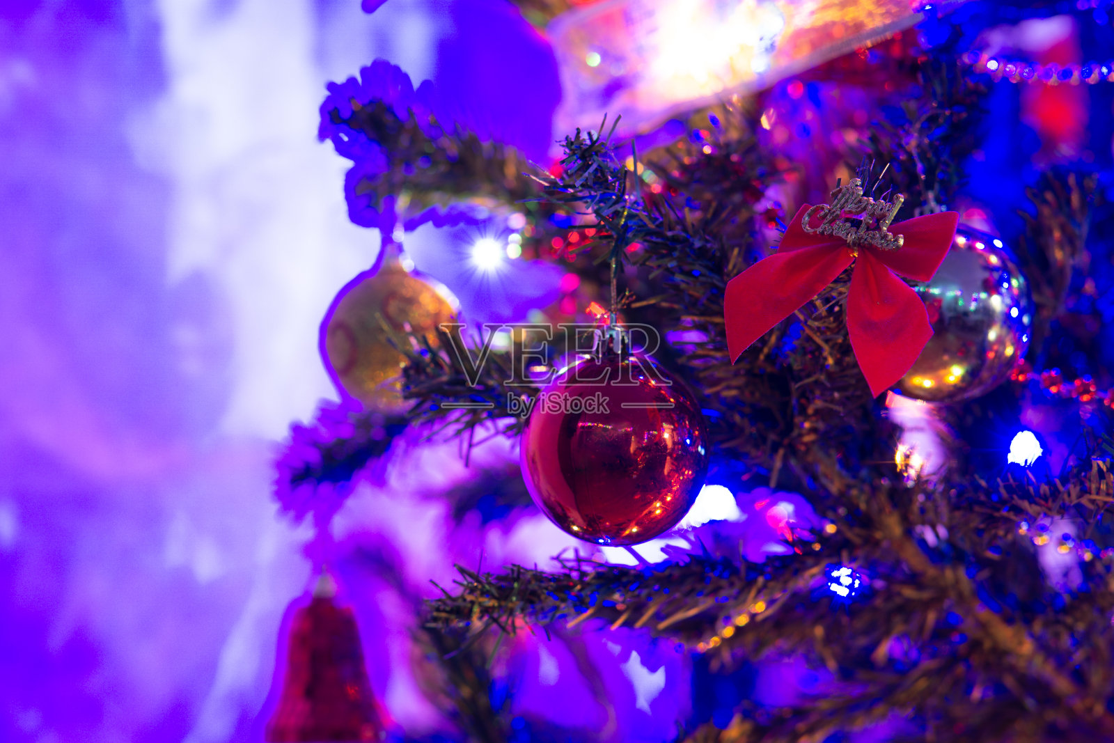 在黑暗的房间里,用红色和金色装饰的圣诞树,用蓝色的圣诞彩灯,复制空间红色的蝴蝶结,在圣诞树上写着“圣诞快乐”照片摄影图片