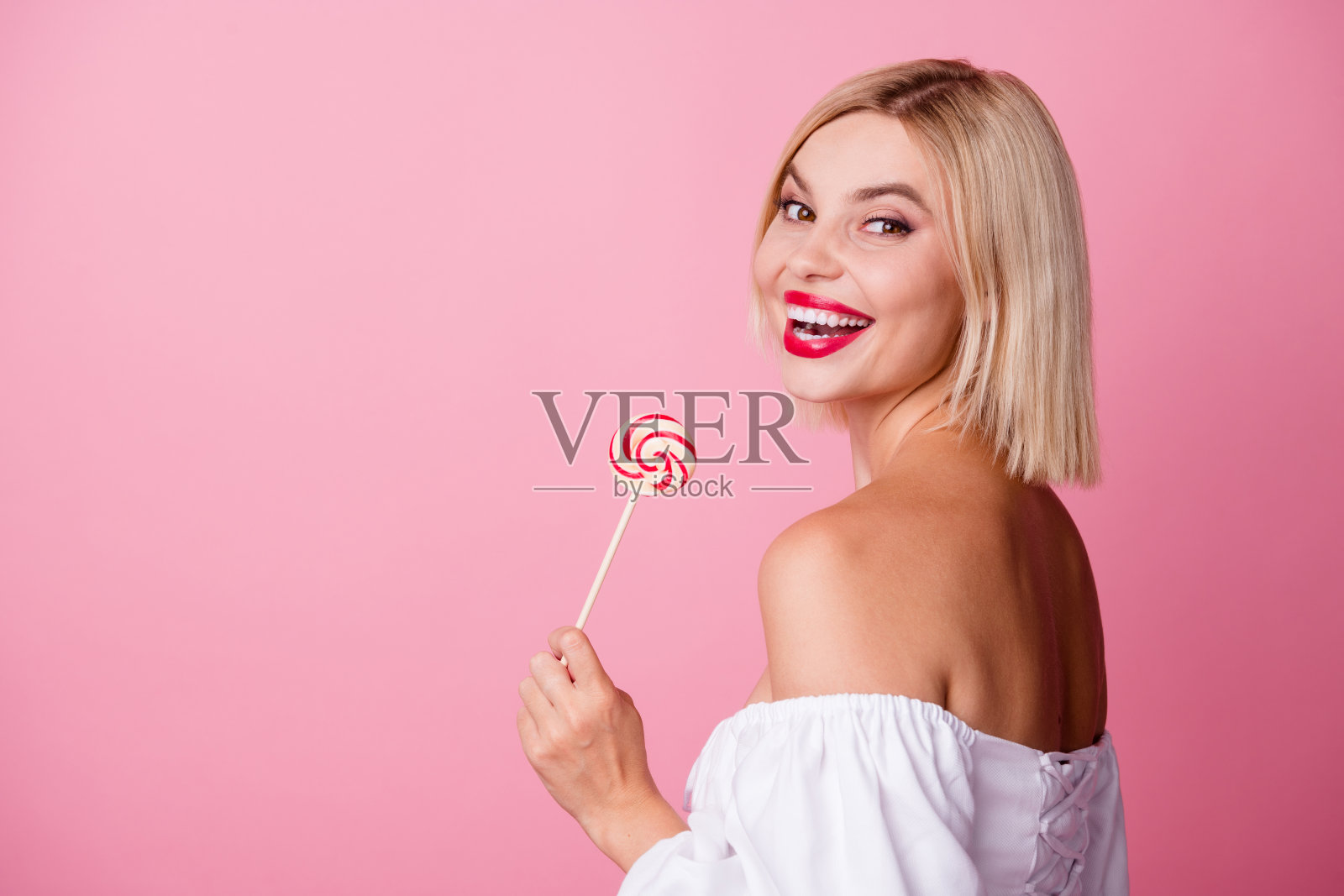 照片中可爱漂亮的女士穿着白色性感连衣裙,手持焦糖棒,空白空间孤立粉红色背景照片摄影图片