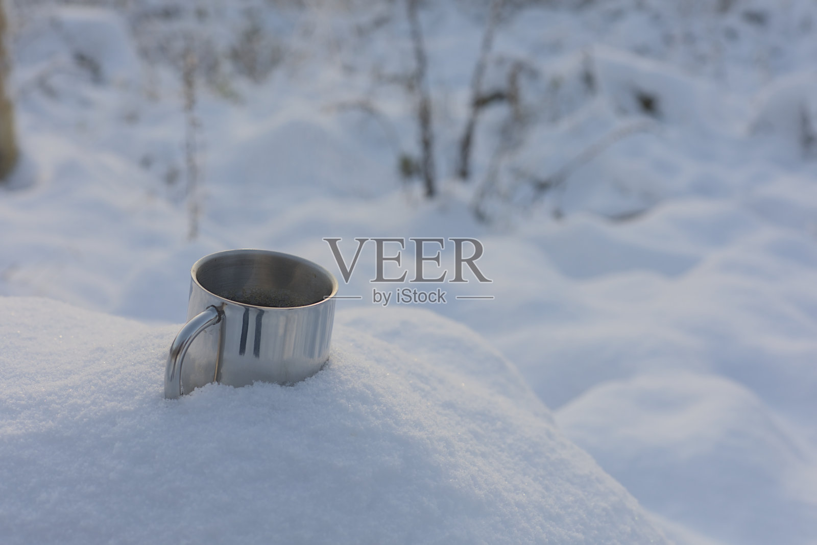 冬天森林里的雪里,金属杯里装着咖啡照片摄影图片