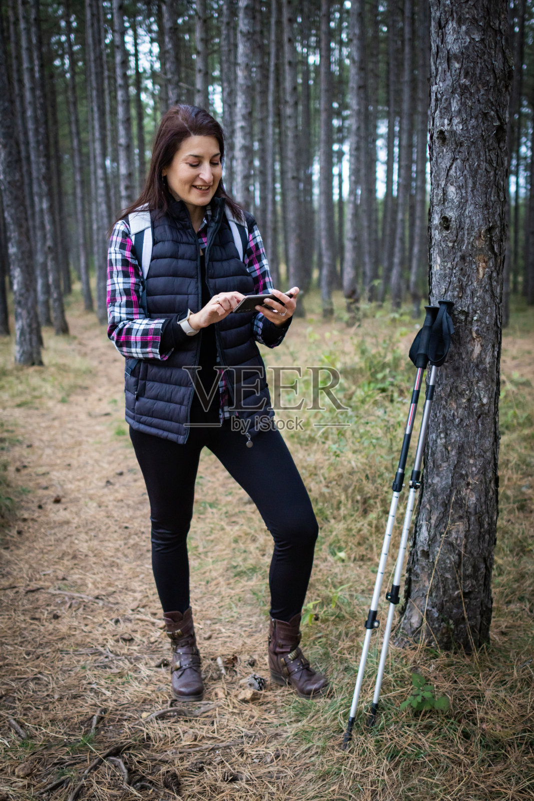 在多云的秋日里,背着背包的女徒步旅行者在大自然中悠闲地散步。健康的户外生活方式。她正在查看在线地图。照片摄影图片