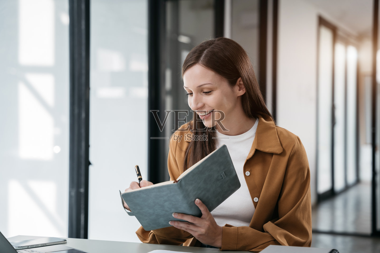 女企业家在早上用智能手机在办公桌上的笔记本上做笔记。照片摄影图片