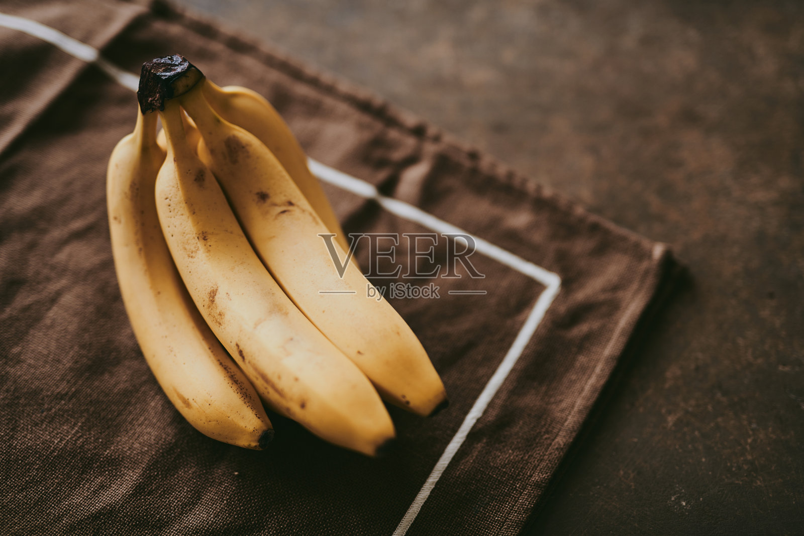 一串香蕉在棕色纹理背景上的特写照片摄影图片