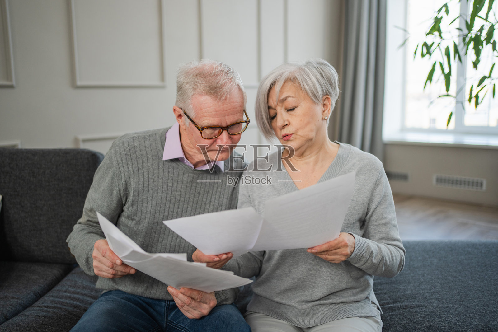 伤心、疲惫、失望的中年老年夫妇拿着纸质文件坐着。不快乐的年长成熟的男人女人阅读纸账单管理银行财务计算税收规划贷款债务养老金支付。照片摄影图片