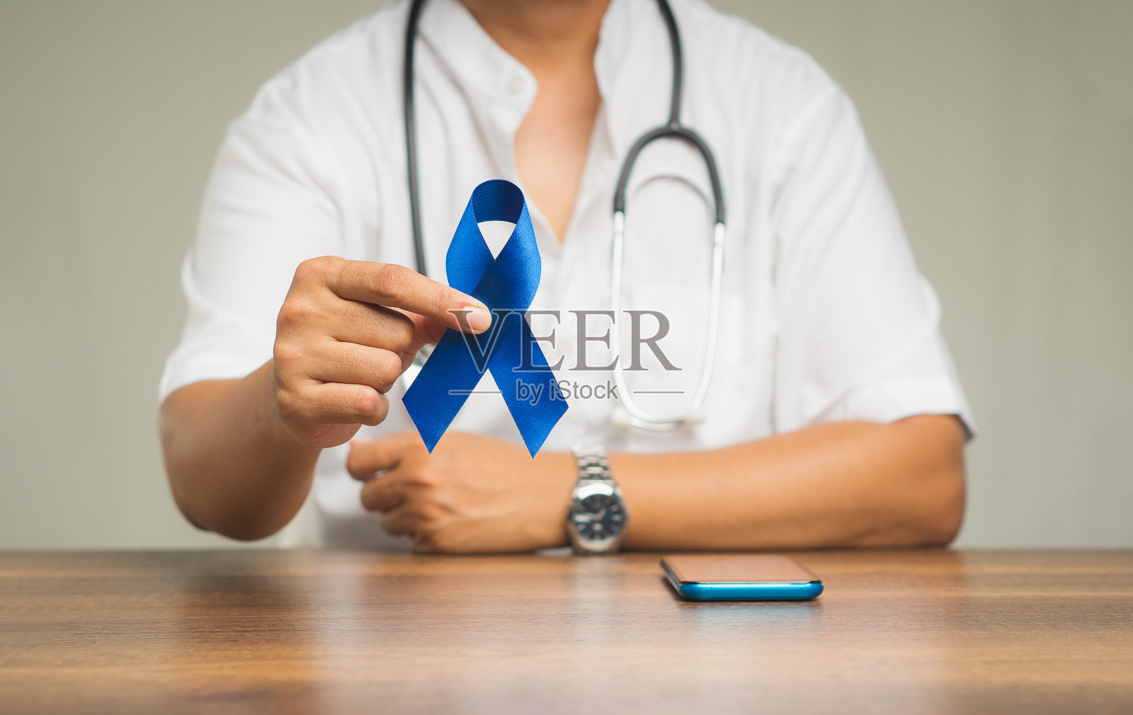 在灰色背景下,一只手拿着蓝丝带的特写。照片摄影图片