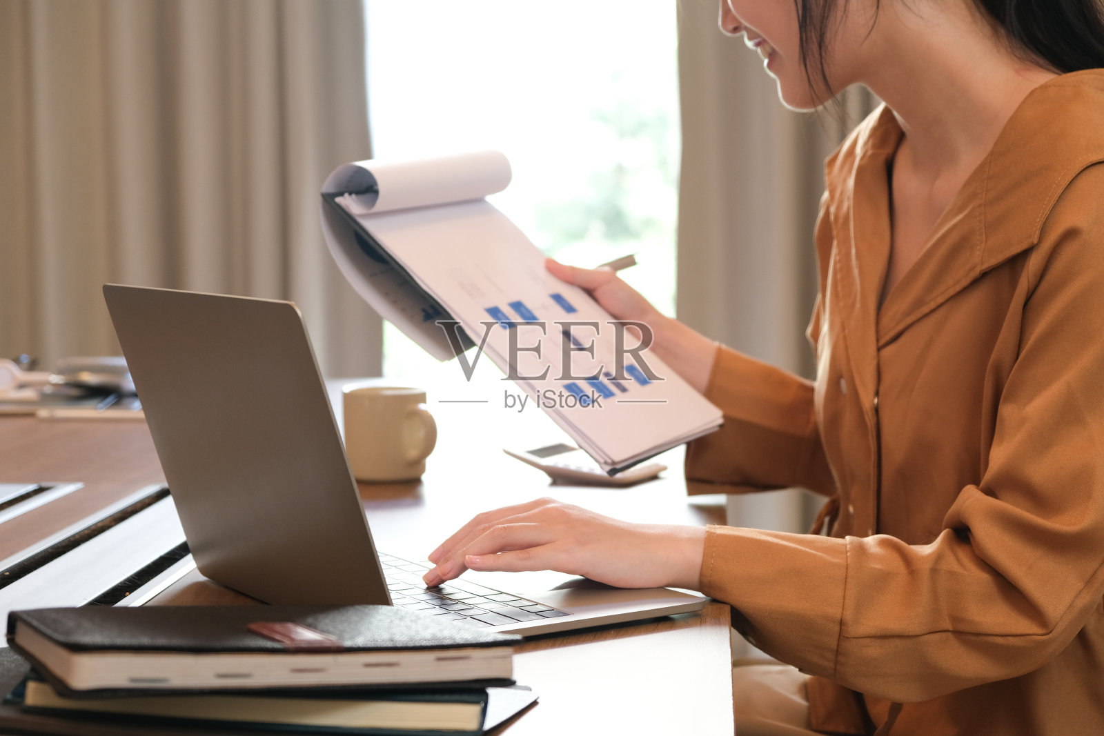 年轻迷人的亚洲女人微笑着思考计划,在笔记本电脑,平板电脑和笔记本电脑上写作,在家工作,看着现代办公室的相机照片摄影图片