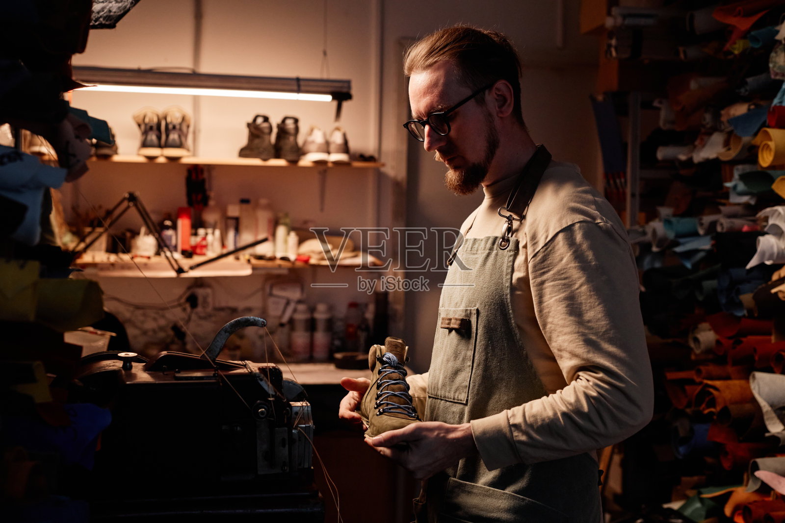 年轻的长着胡子的鞋匠的侧视图,手里拿着靴子工件照片摄影图片