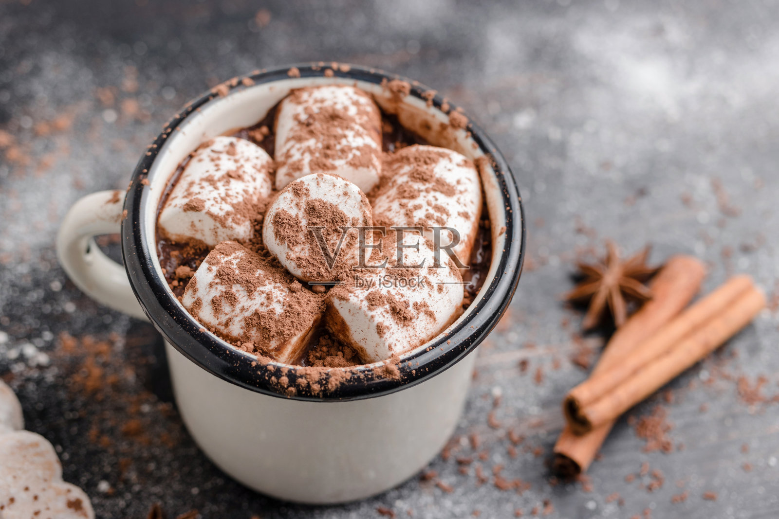 自制的香辣热巧克力饮料,白色棉花糖装在搪瓷杯里,放在木桌上,配上肉桂棒、饼干和八角茴香照片摄影图片