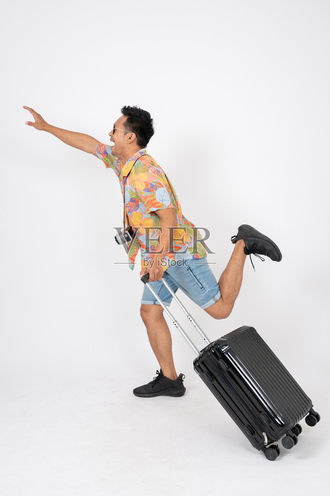 一个兴奋的亚洲男子游客穿着夏装,带着行李在跳,孤立的背景。照片摄影图片