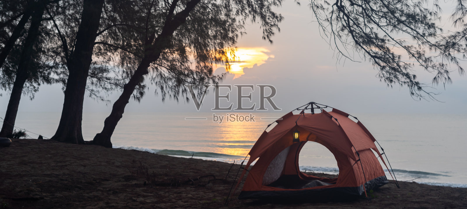 在初升的太阳下,在海边的沙滩上搭帐篷露营。照片摄影图片