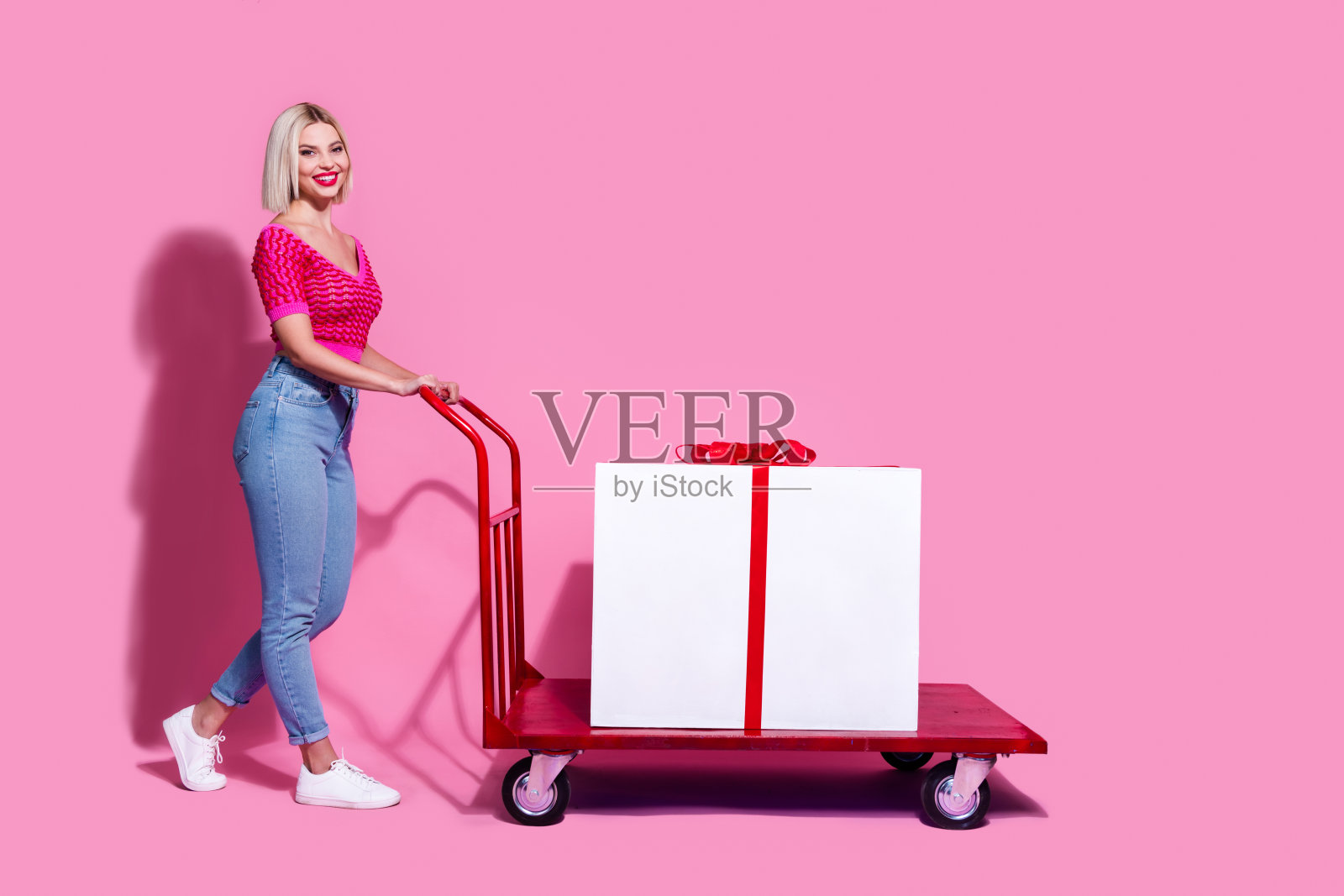 华丽的女人的全身照片穿着针织品衣服牛仔裤推车与大礼物到空白的空间孤立在粉红色的背景照片摄影图片