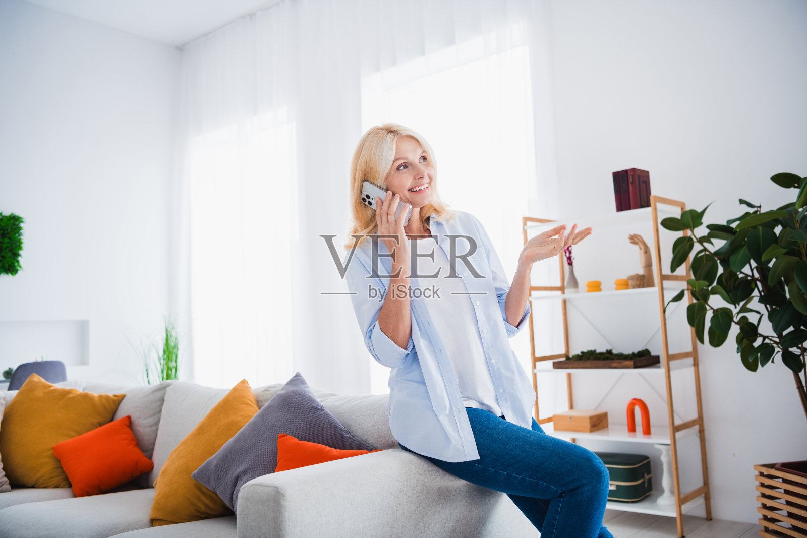 金发正放松自信的女士在家里的客厅公寓里独自打电话聊天,看起来很好奇照片摄影图片