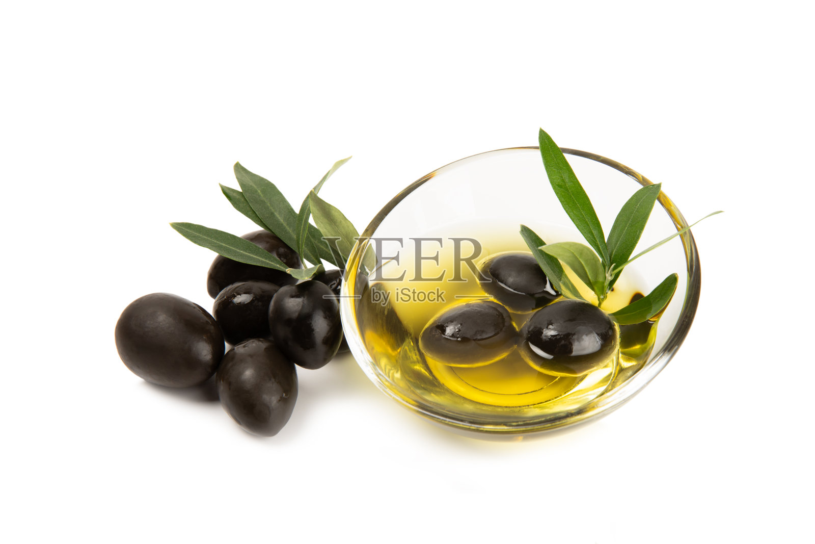 一碗新鲜的橄榄油和橄榄,在白色的背景上孤立的叶子。玻璃碗里装着美味的橄榄油。橄榄油瓶。照片摄影图片