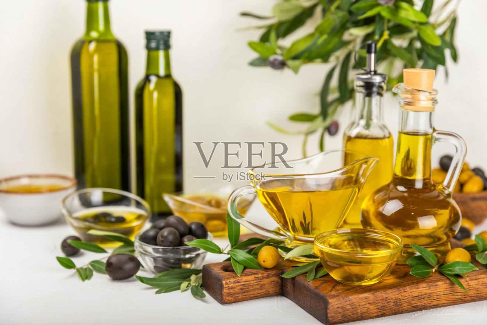 白色纹理背景上的一瓶橄榄油。油瓶上有树枝和橄榄果实。放文字的地方。副本的空间。食用油和沙拉酱。照片摄影图片