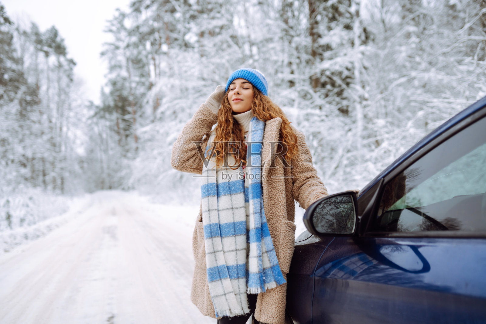 美丽的年轻女子在雪地里的一辆车旁。照片摄影图片