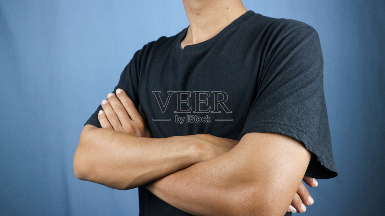 在蓝色背景上,一个穿着黑色衬衫,双臂交叉的男人照片摄影图片