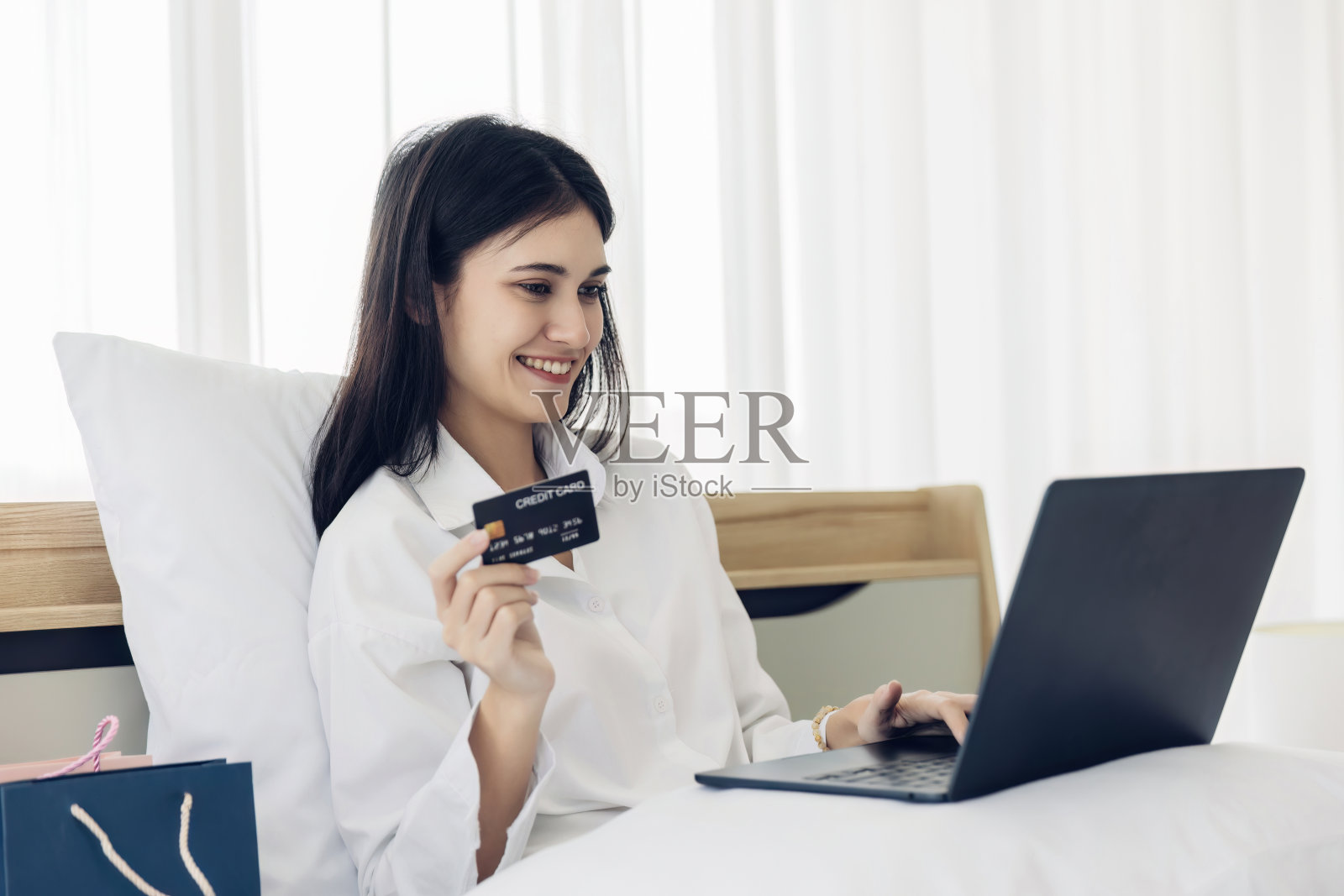 快乐的女人在家里的卧室里网购。女人在家放松地躺在床上用智能手机发短信,微笑的女孩在家用手机网购照片摄影图片