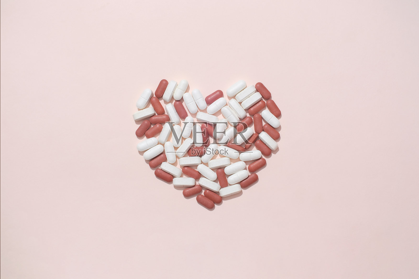 白色和红色的药片在粉红色的背景上排成心形。片剂是一种固体形式的药物,其组成包括药物成分和赋形剂。照片摄影图片