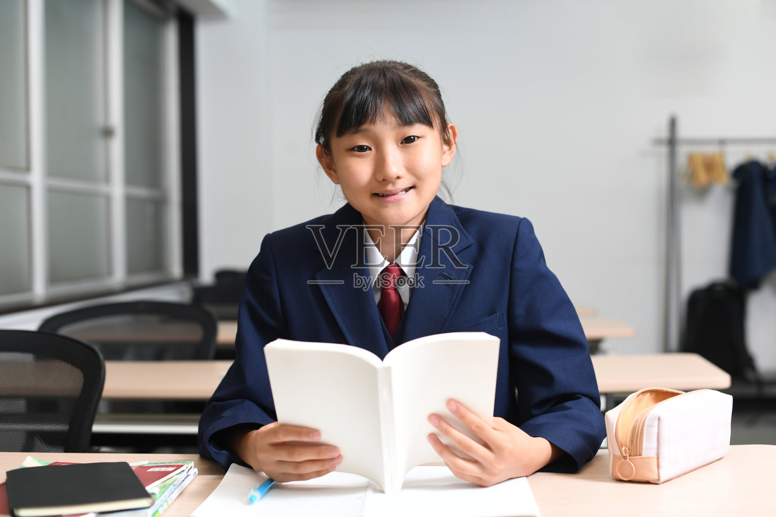 穿着制服的亚洲女学生在教室里拿着课本学习照片摄影图片