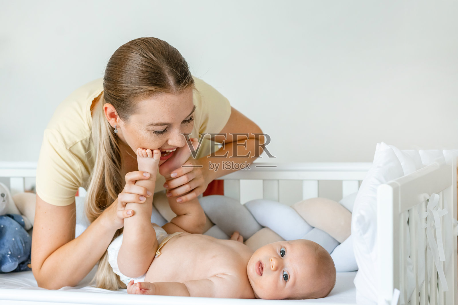 微笑的年轻母亲在家里卧室的床上玩着小男孩的腿。慈爱的妈妈享受着照顾和教育孩子的乐趣。健康的儿童保育。照片摄影图片