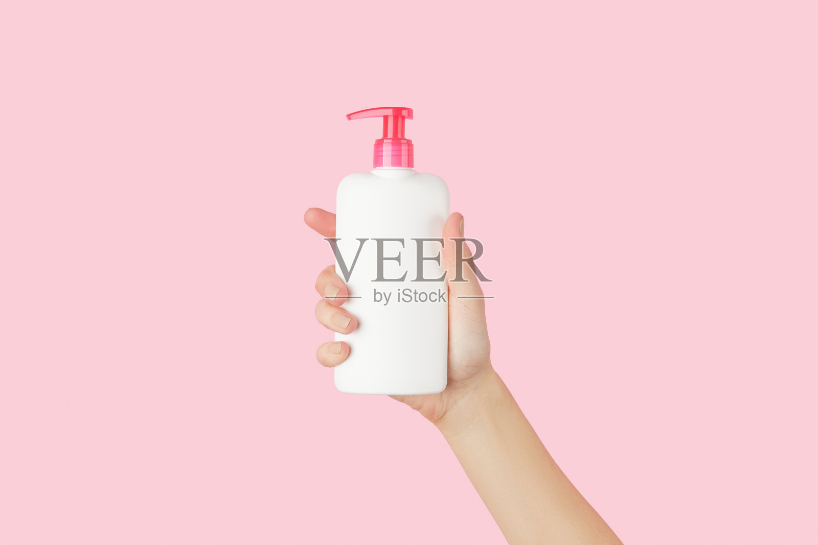 女人的手拿着淡粉色背景的白色瓶子照片摄影图片