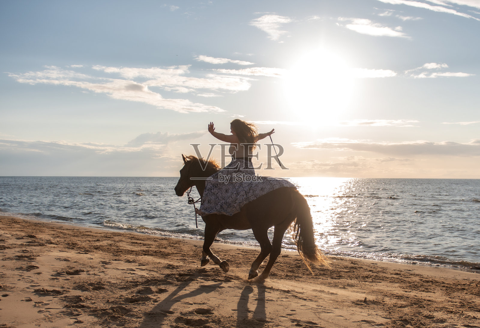一个年轻的成年女子在阳光明媚的日子里愉快地在海滩上骑马照片摄影图片