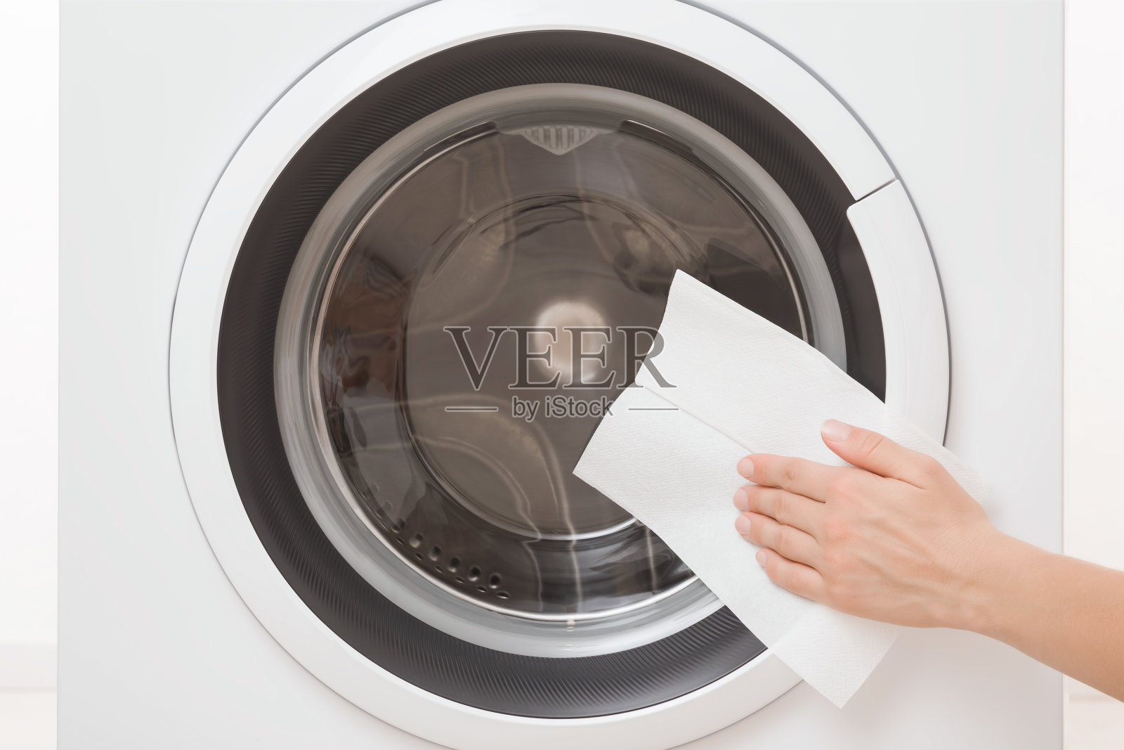 年轻的成年妇女用手用干纸巾和擦玻璃门外的白色洗衣机表面。特写镜头。定期清理。前视图。照片摄影图片