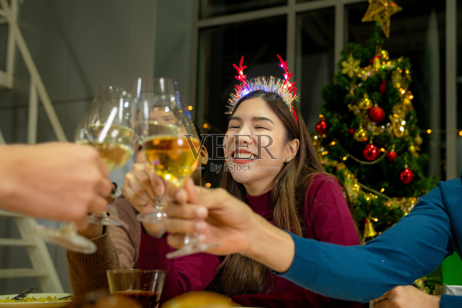 近距离观看带有灯光的叮当作响的香槟酒杯。喝香槟的晚宴。手里拿着清澈的玻璃杯,酒精在黄色的映照下闪闪发光。照片摄影图片