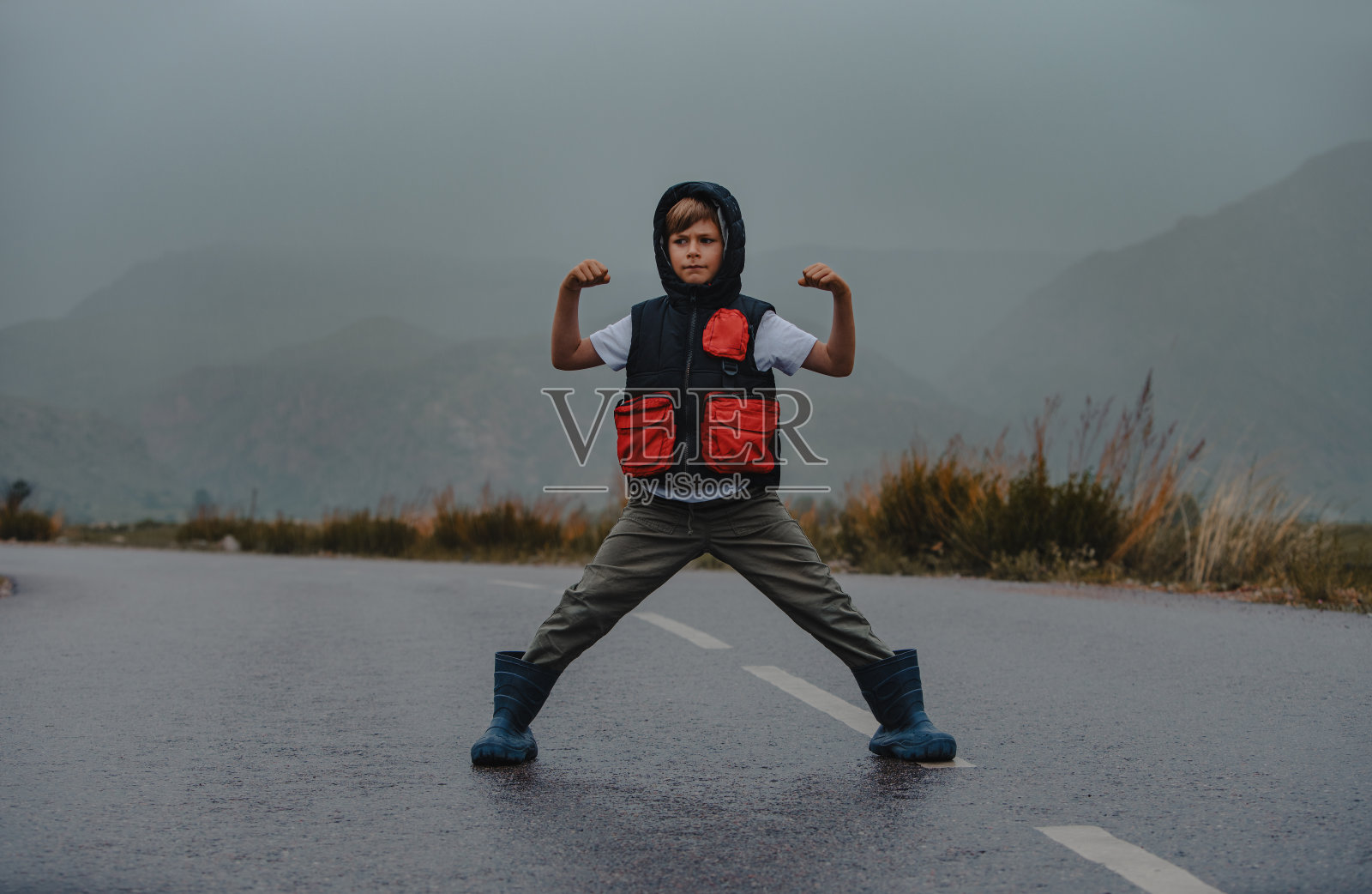 一个男孩以英雄的姿态站在雨天的柏油路上照片摄影图片
