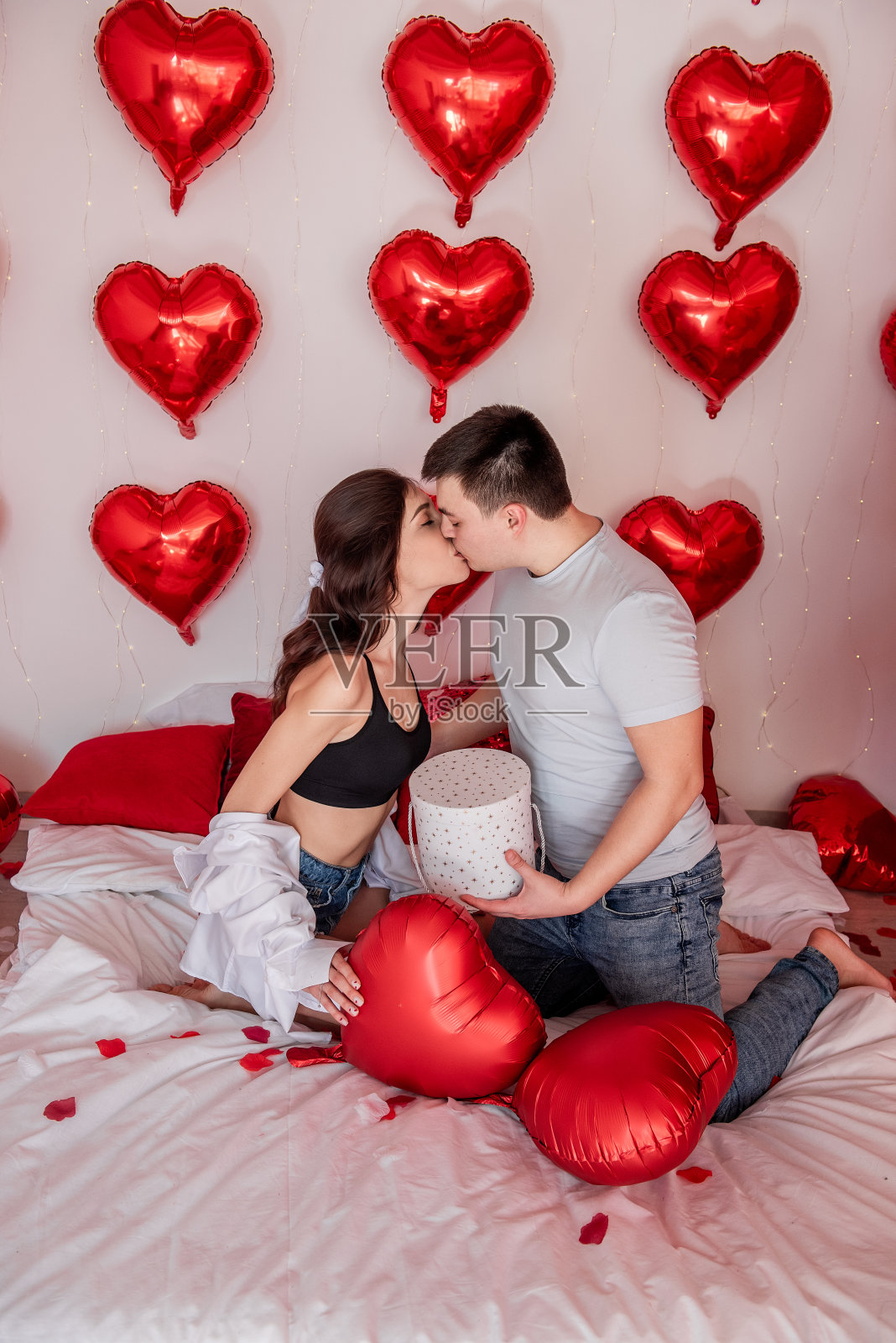 一对情侣坐在装饰着心形气球的床上接吻。情人节照片摄影图片