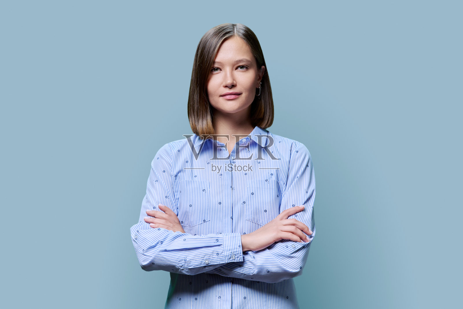 蓝色背景上自信的年轻女子双臂交叉的肖像照片摄影图片