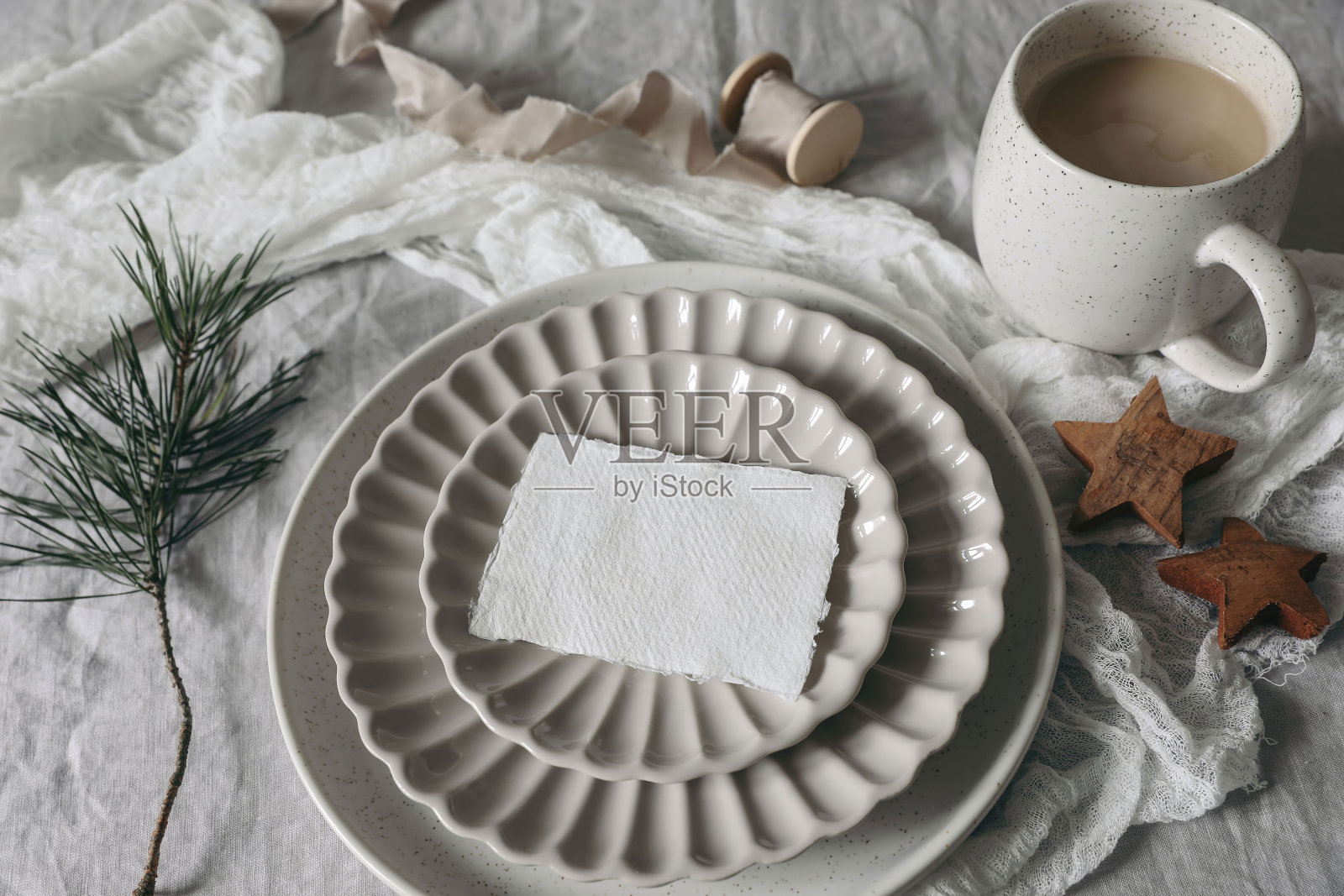 圣诞节静物画。空白名片,邀请模型在陶瓷板上。白色亚麻桌布上的木制星星和松树树枝。一杯咖啡,冬日的早餐。节日假期平铺照片摄影图片