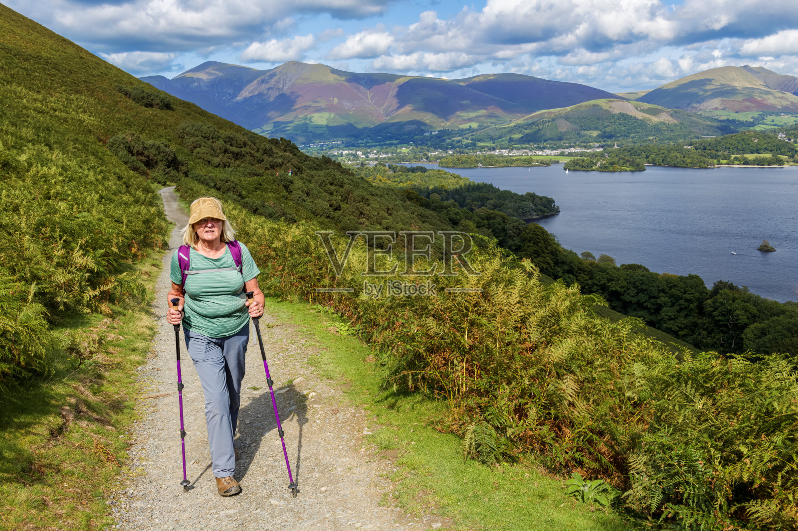 在英国坎布里亚郡的湖区,一名老年女性徒步旅行者在德文特水域周围的环形步道上拄着拐杖。照片摄影图片
