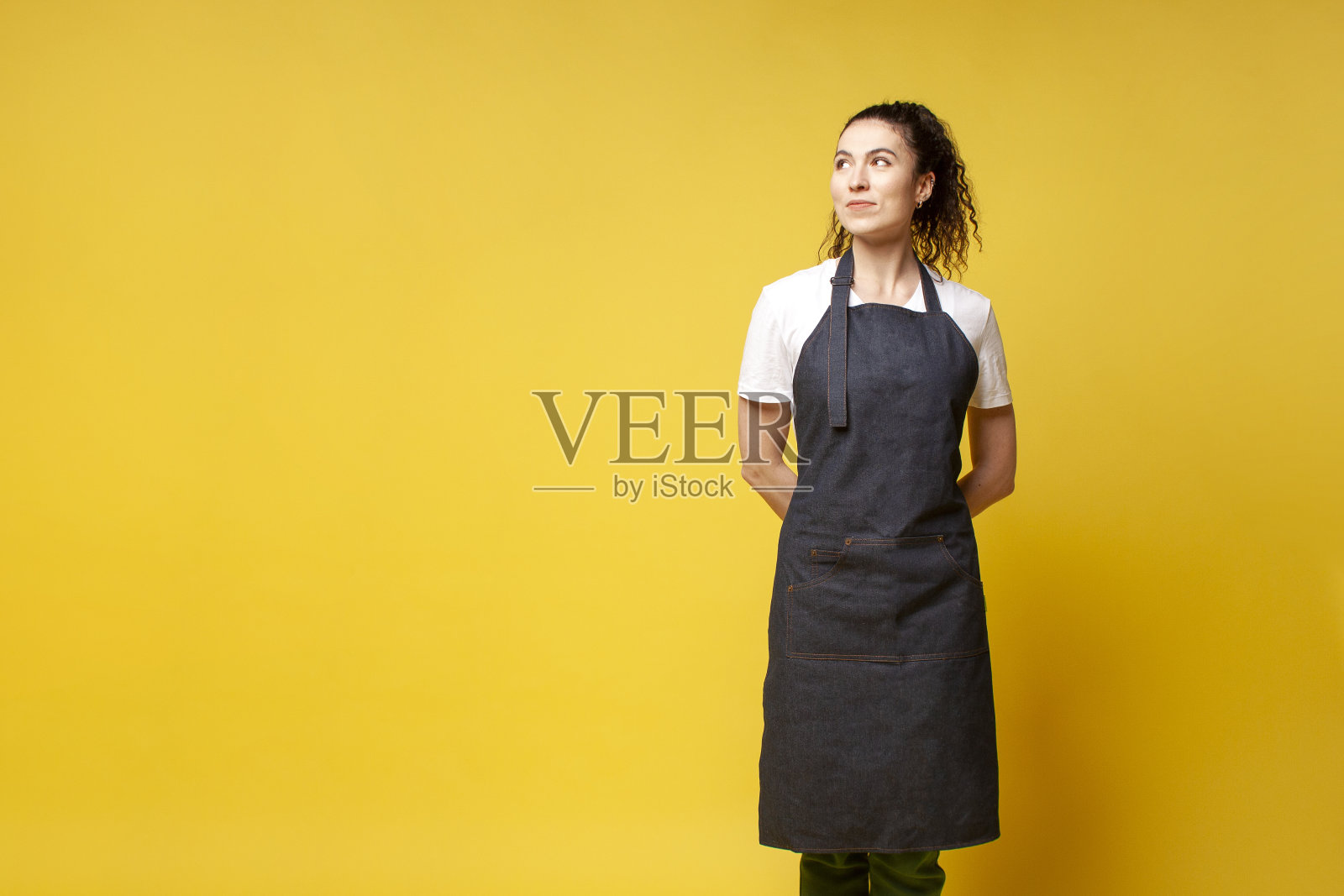 穿着制服的女服务员站在那里,双手放在背后,看着别处,咖啡女服务员穿着牛仔围裙照片摄影图片