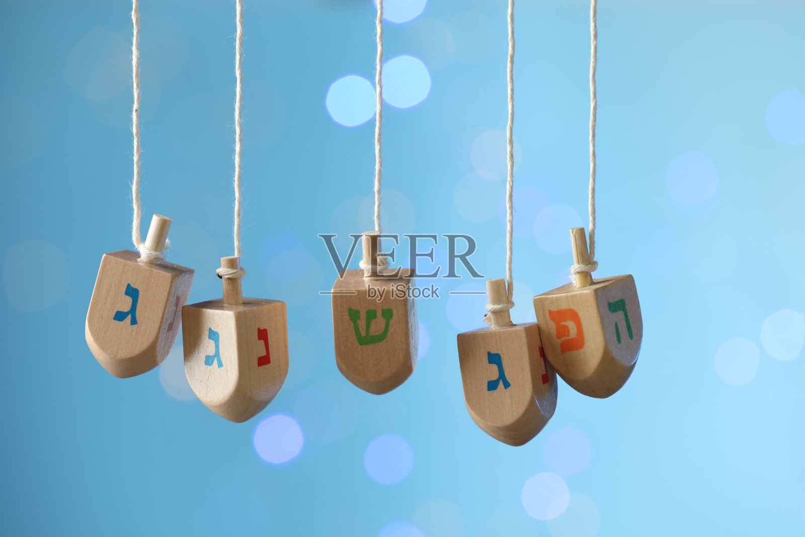 光明节的庆祝活动。带有犹太字母的木制卷轴挂在麻绳上,淡蓝色的背景上有模糊的灯光照片摄影图片