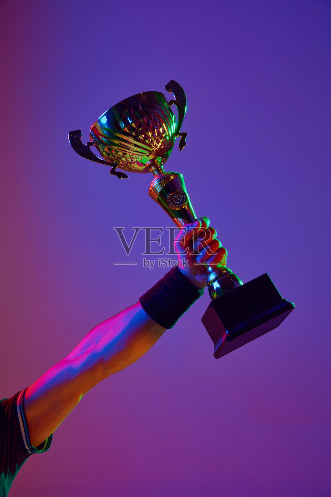 在霓虹灯的渐变工作室背景下,男性手持奖杯。赢家,冠军,成功照片摄影图片