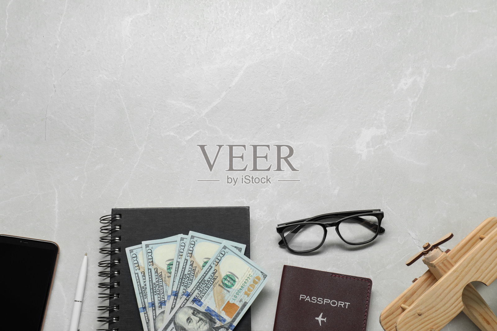 用美元、护照和飞机的木制模型平铺在浅色大理石桌上,为文字留出空间。商务旅行照片摄影图片