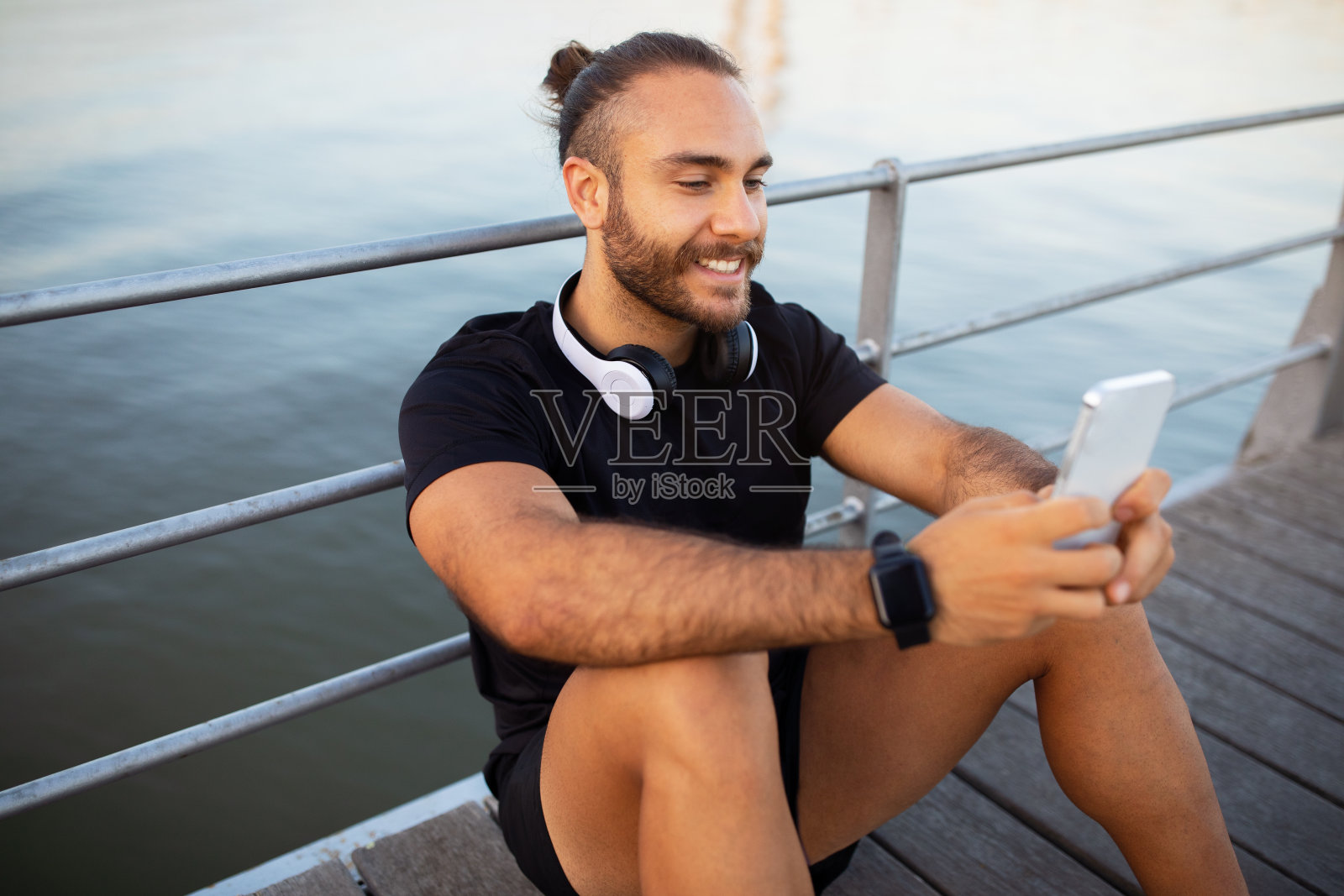 快乐的运动员,戴着耳机,坐在户外用智能手机发短信照片摄影图片