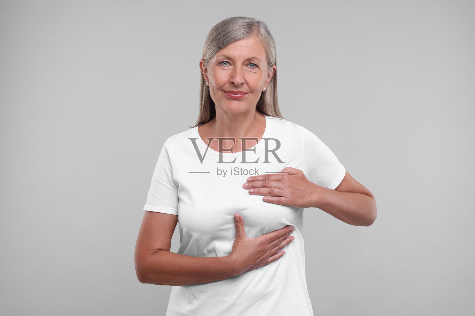 美丽的老年妇女在浅灰色背景上做乳房自我检查照片摄影图片