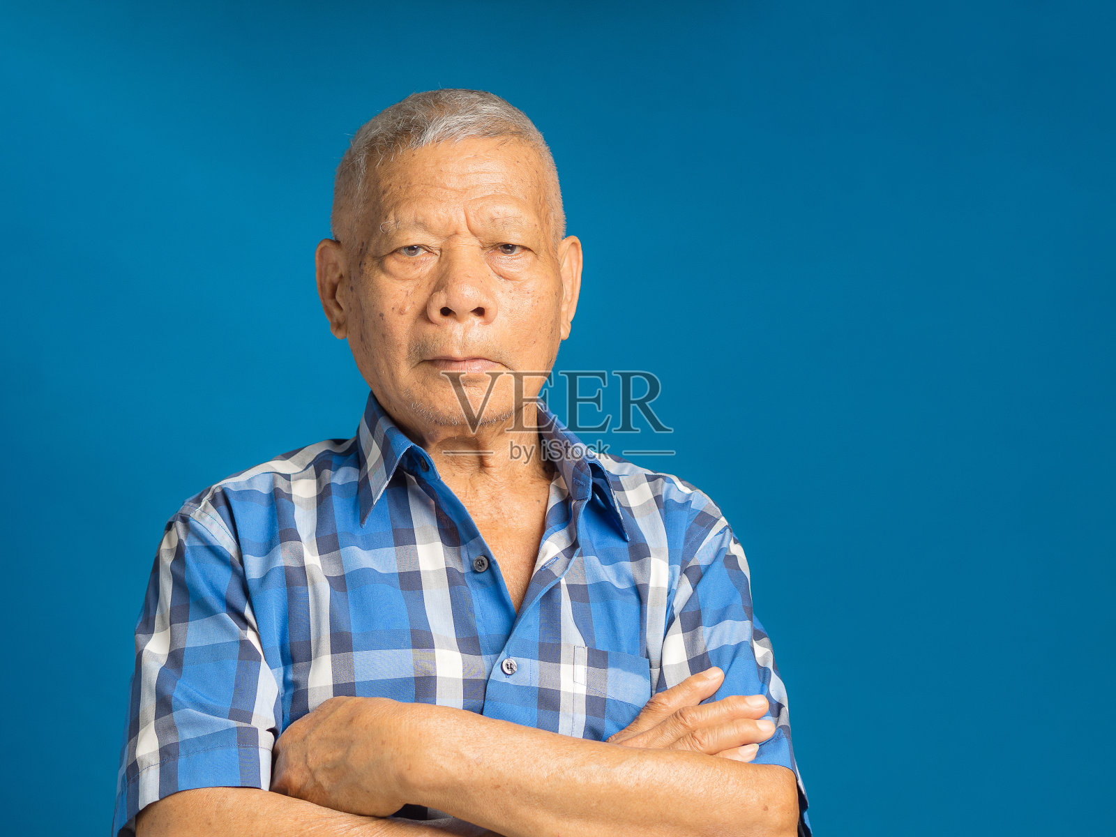 一位年长的男子站在蓝色背景上,双臂交叉地看着镜头照片摄影图片