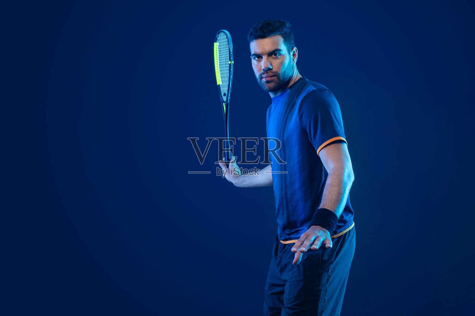 在壁球场上拿着球拍的壁球运动员。男运动员在球场上拿着霓虹色的球拍。体育的概念。下载一张高质量的照片,用于设计体育应用程序或博彩网站。照片摄影图片