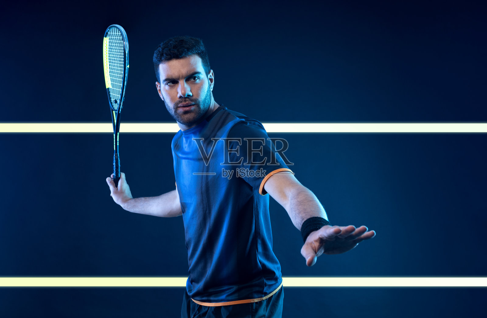 在壁球场上拿着球拍的壁球运动员。男运动员在球场上拿着霓虹色的球拍。体育的概念。下载一张高质量的照片,用于设计体育应用程序或博彩网站。照片摄影图片