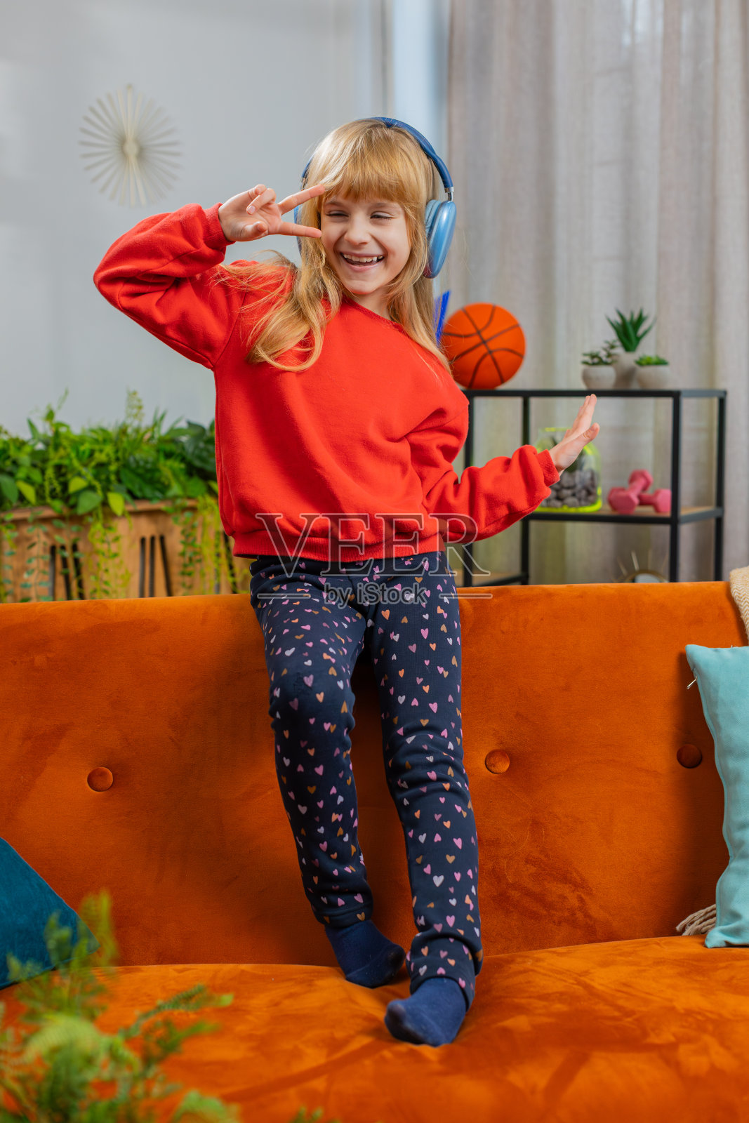 快乐的小女孩戴着无线耳机,坐在家里的沙发上听着喜欢的音乐照片摄影图片