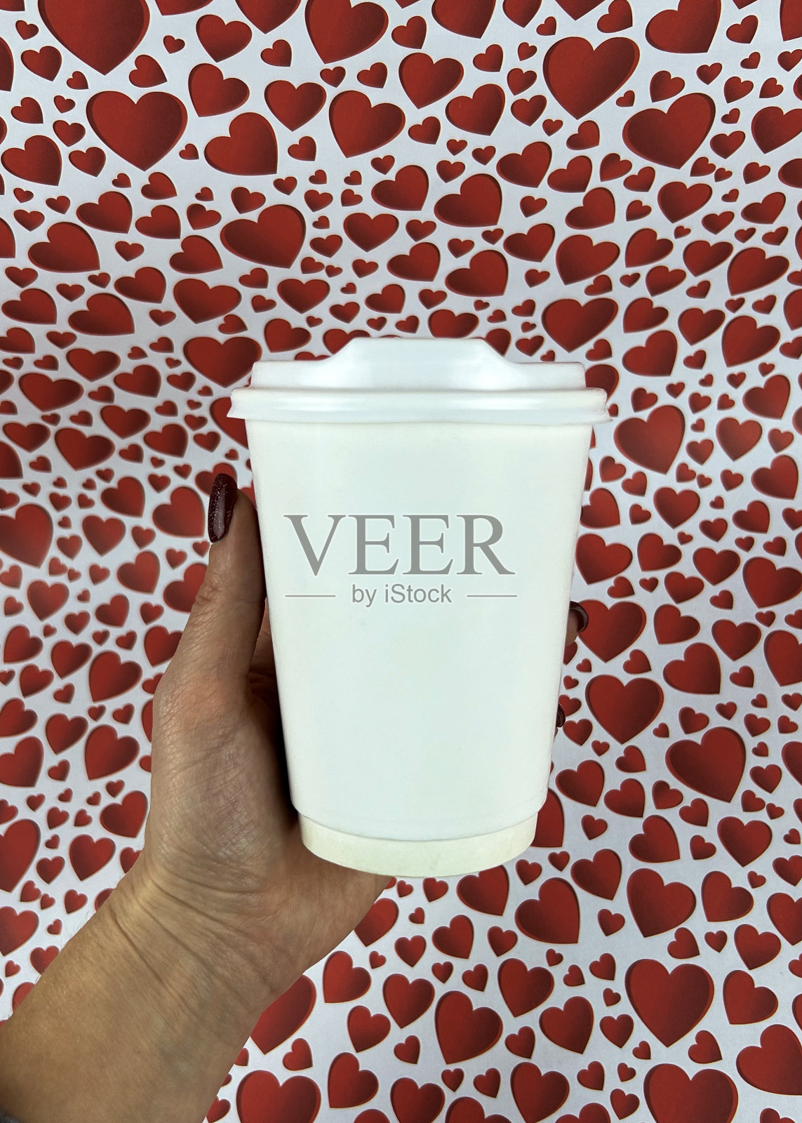 一个女人手里拿着一个白色纸杯,背景是红心。情人节概念照片摄影图片