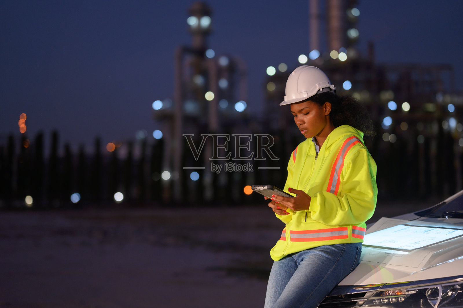 身穿制服、戴着钢盔的女工程师,负责检查绿色印刷工程和无线电通讯检查,有炼油厂背景的施工现场。照片摄影图片