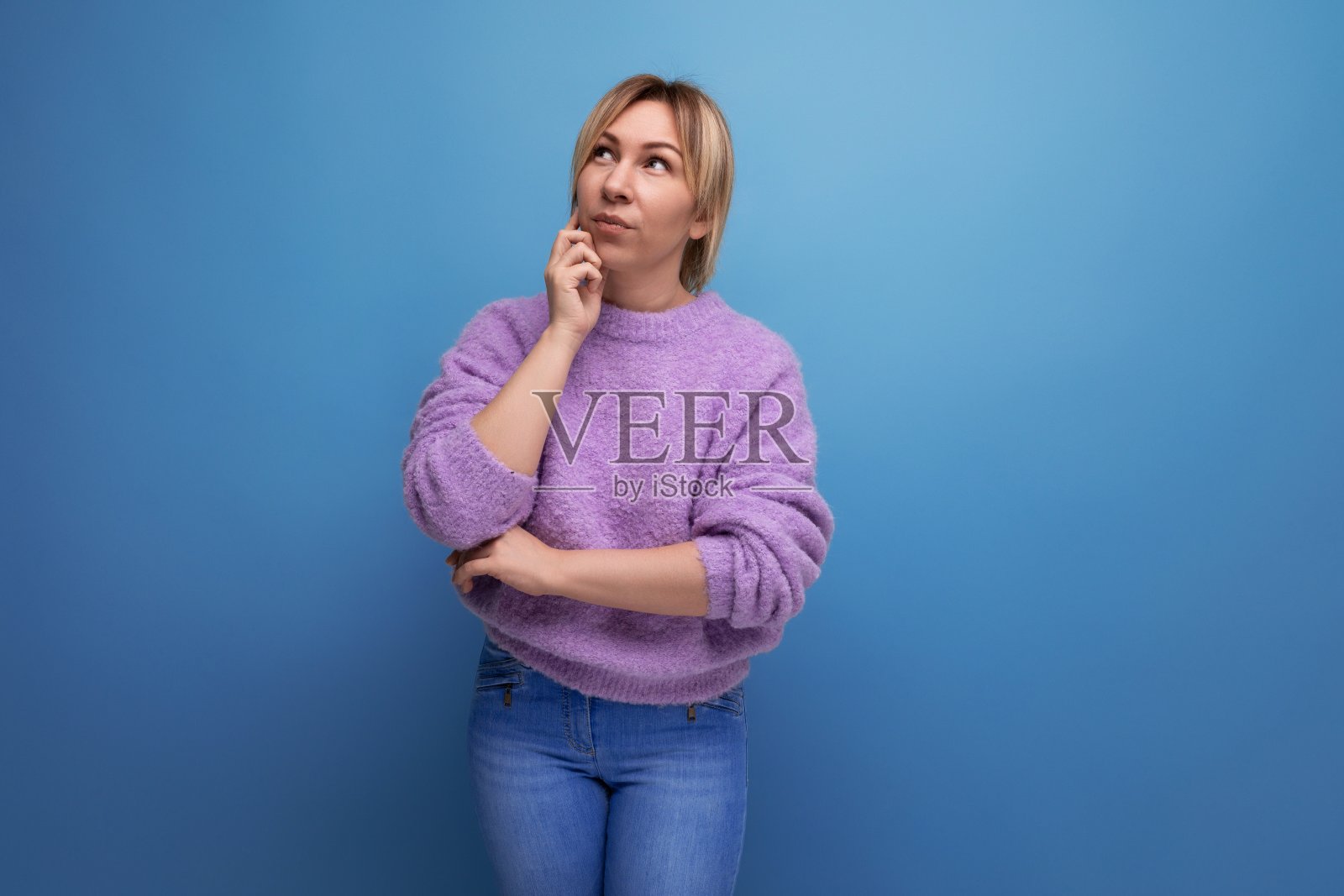 在明亮朴素的背景上,一个忧郁悲伤的金发年轻女子身穿淡紫色毛衣照片摄影图片